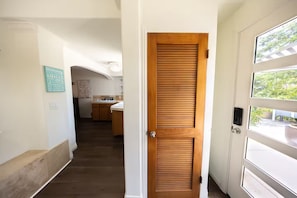 A hallway leading to a wooden door, a kitchen area with wooden cabinets, and a welcome sign on the wall. - Solana Beach Bungalow (Solana Beach)