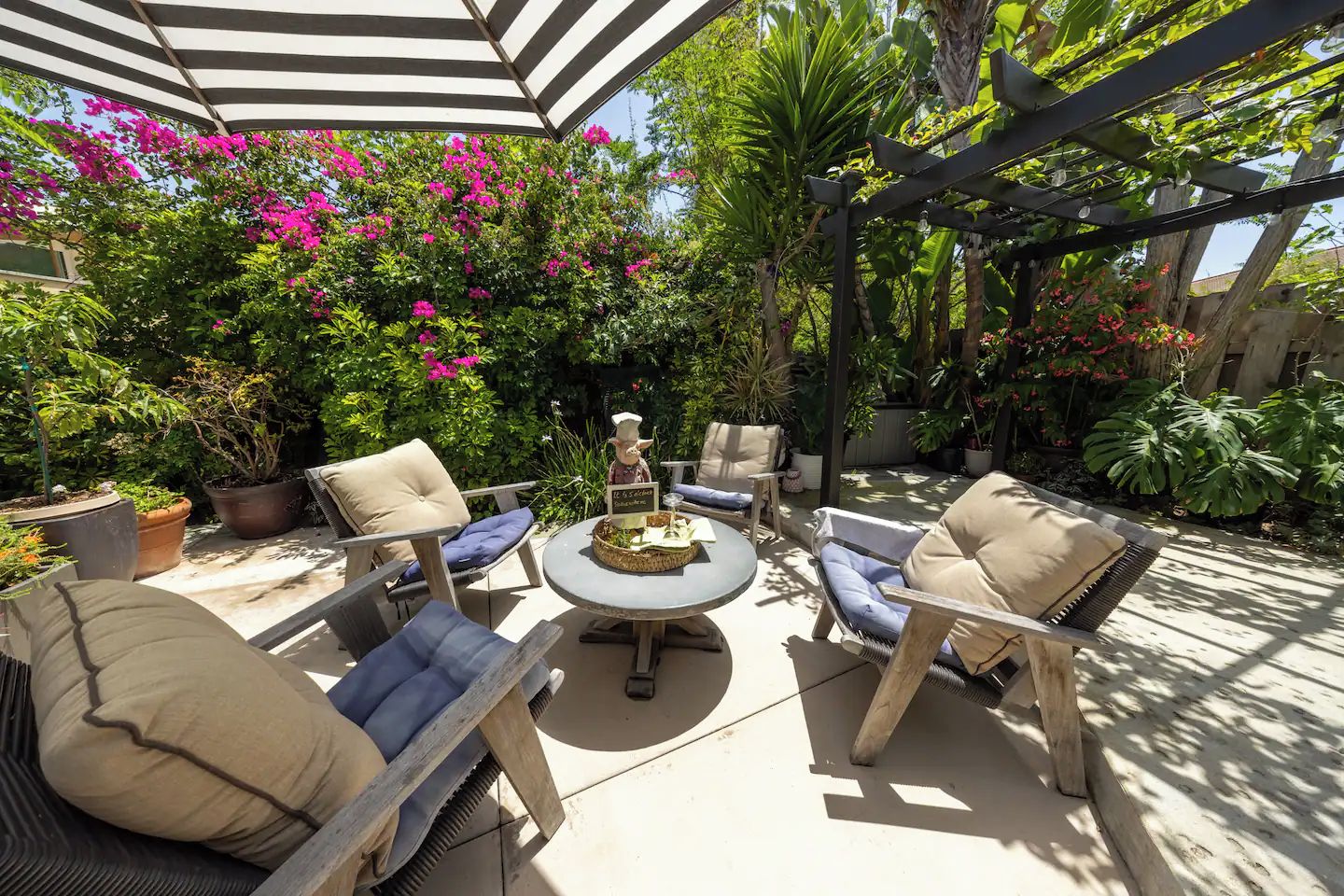 Un patio exterior con una mesa redonda, cuatro sillas y una pérgola con toldo a rayas.