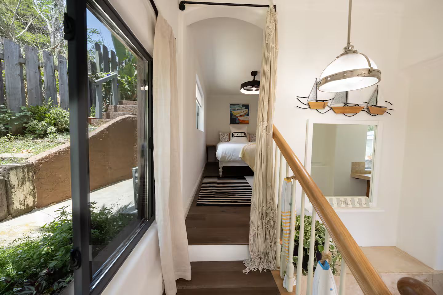 A hallway with a bed, macramé wall hangings, and a staircase leading to another room.