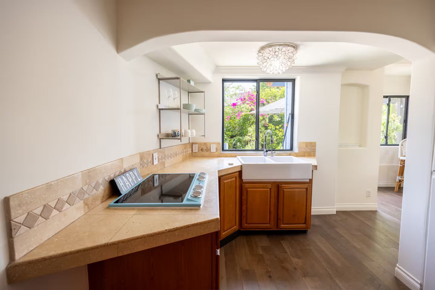 A kitchen with a built-in stove, a sink, wooden cabinets, and a window with a view of greenery.