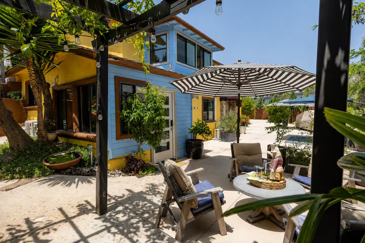 A patio area with outdoor furniture, a striped umbrella, and potted plants.