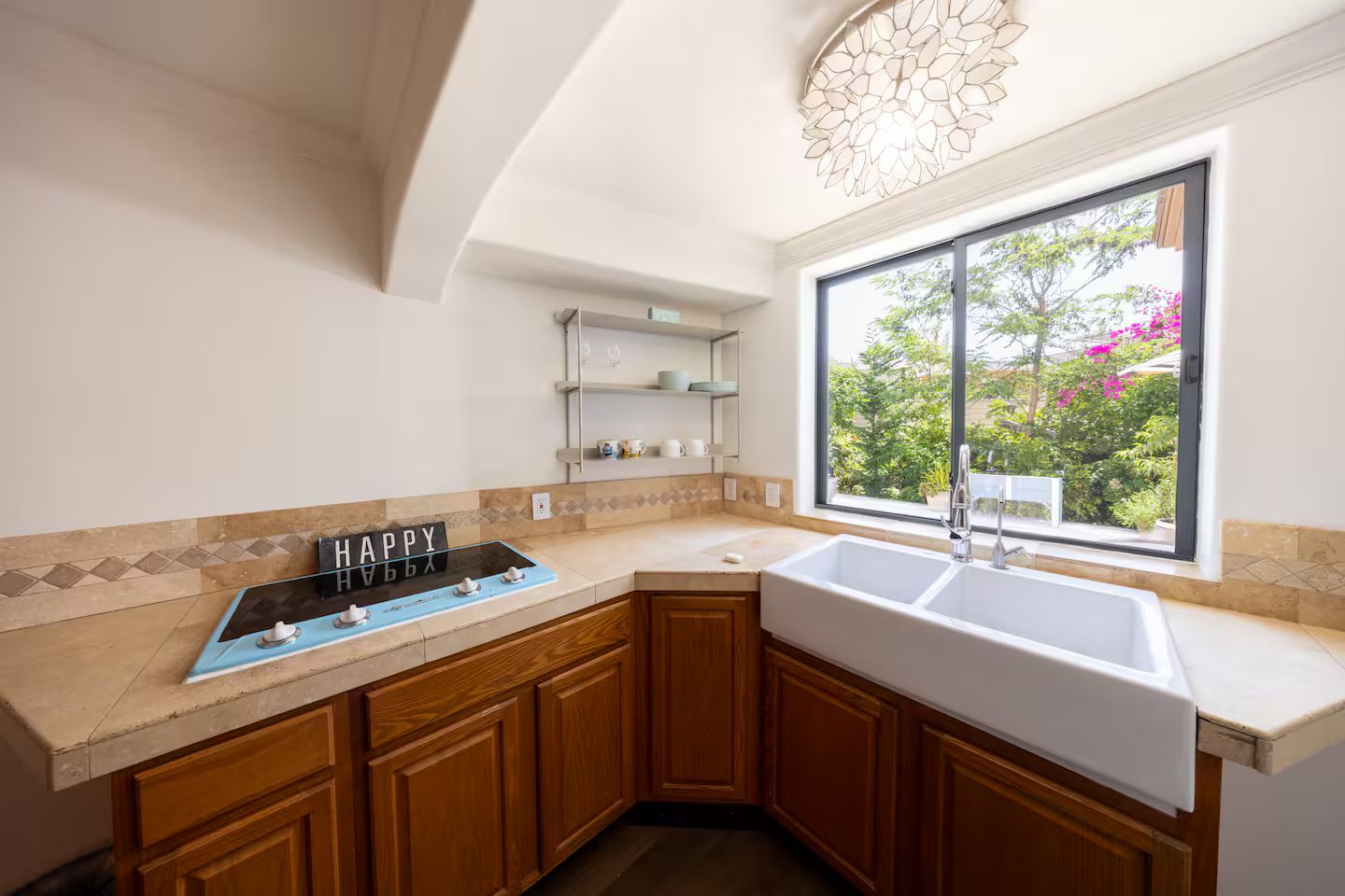 A kitchen with a built-in stove, a sink, wooden cabinets, and a window with a view of greenery.