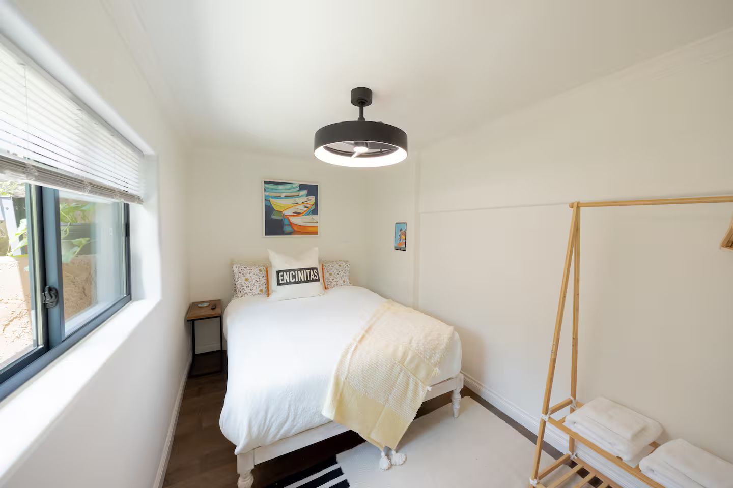 A bedroom with a bed, a bedside table, a window, a hanging light fixture, and a towel rack.
