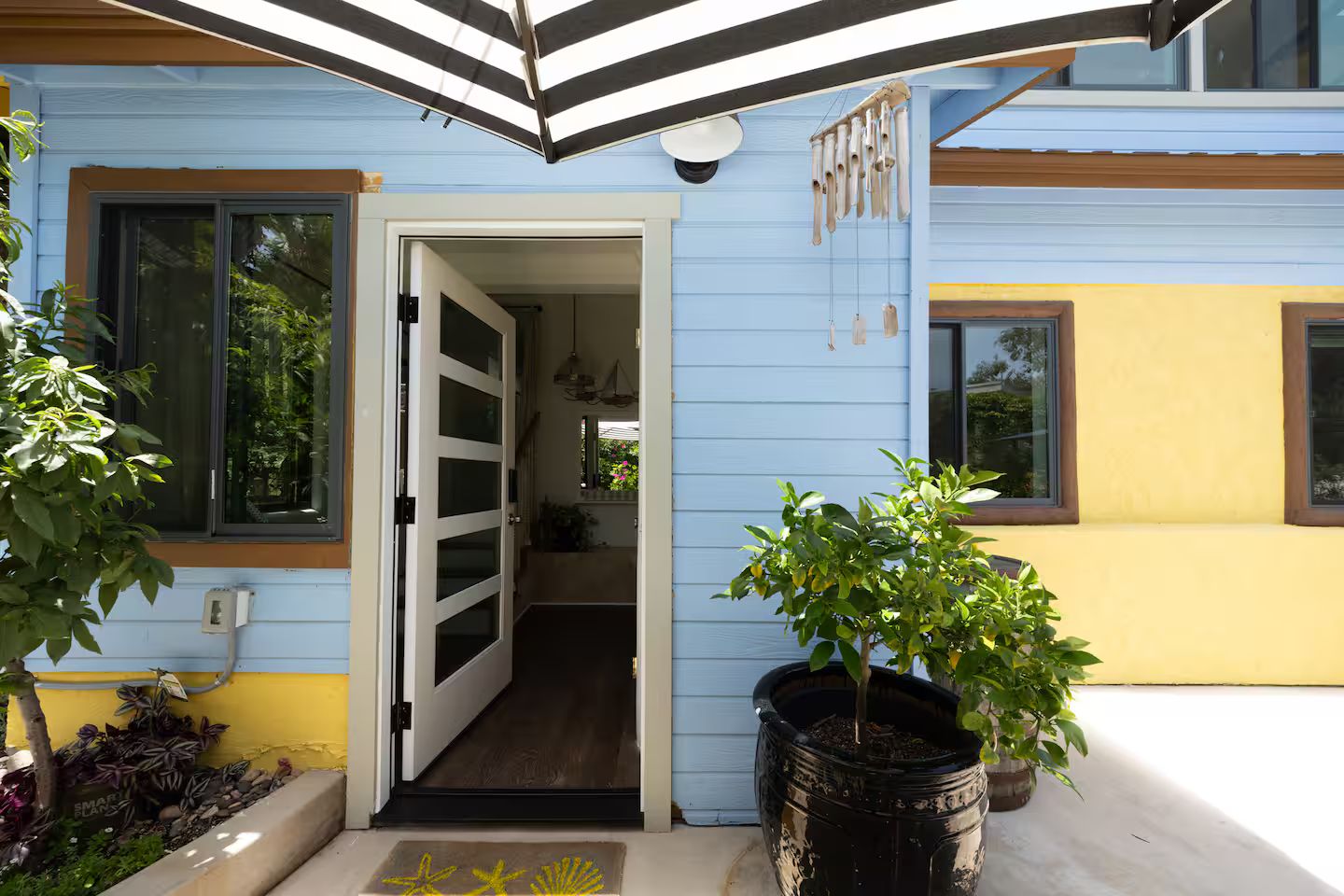 Una casa azul con una puerta blanca, una planta en maceta y un felpudo con estampado de estrella de mar.