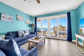 Ein Wohnzimmer mit einer Couch, einem Couchtisch und Blick auf den Strand durch große Glasfenster.