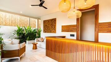 Un área de recepción moderna con un mostrador de madera, un ventilador de techo y lámparas colgantes de mimbre.