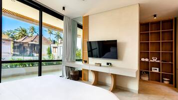 Un dormitorio moderno con una cama grande, un televisor montado en un mueble blanco y vistas a palmeras a través de amplias ventanas.