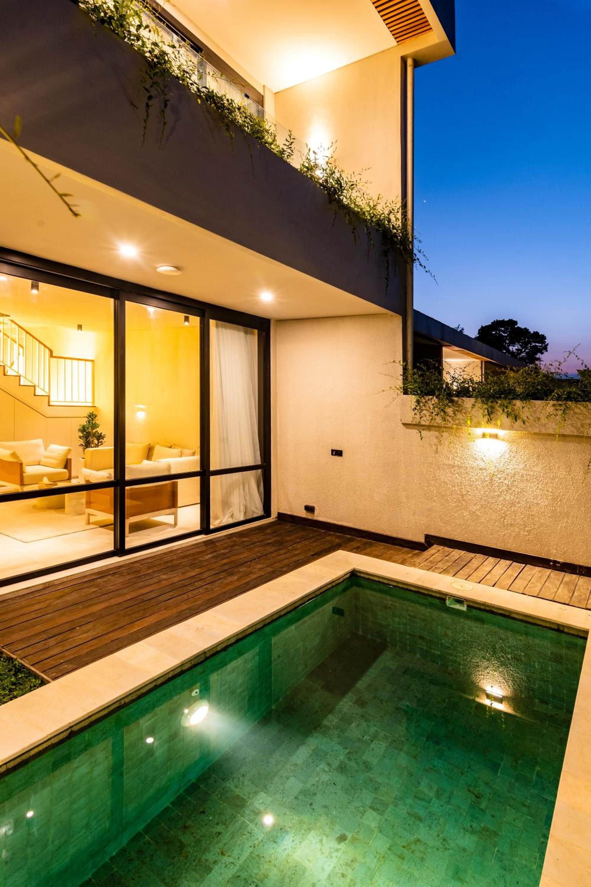 Una casa moderna con piscina, puerta de vidrio que da a un área de estar con sofá y lámpara, y una escalera.