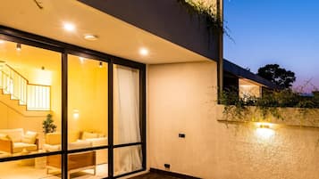 Una casa moderna con piscina, puerta de vidrio que da a un área de estar con sofá y lámpara, y una escalera.
