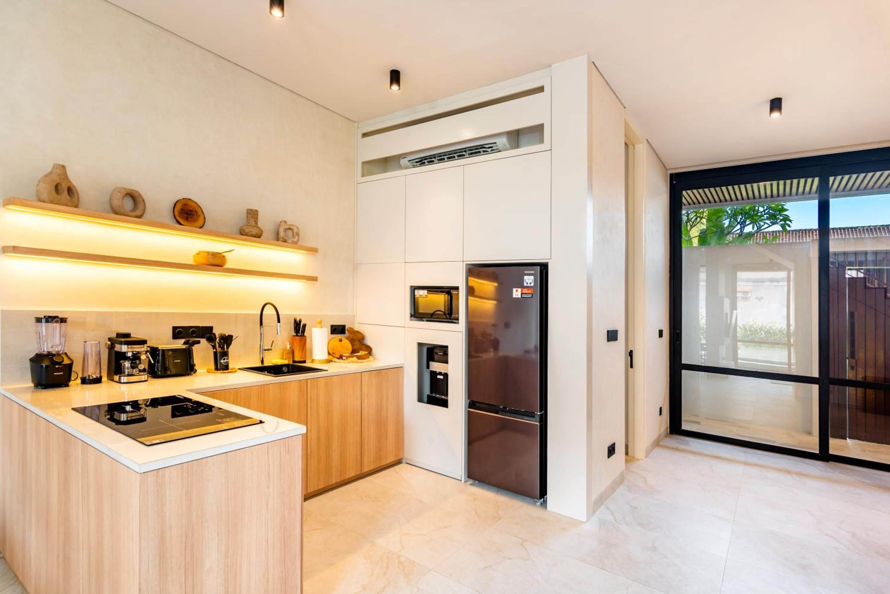 Una cocina moderna con una isla central, electrodomésticos integrados y un amplio ventanal corredero que da a un espacio exterior.