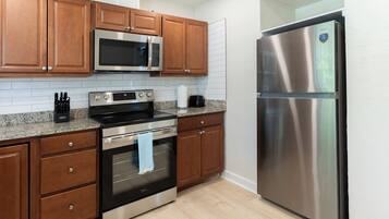 A kitchen with wooden cabinets, a stainless steel refrigerator, a microwave, an oven, and a granite countertop.