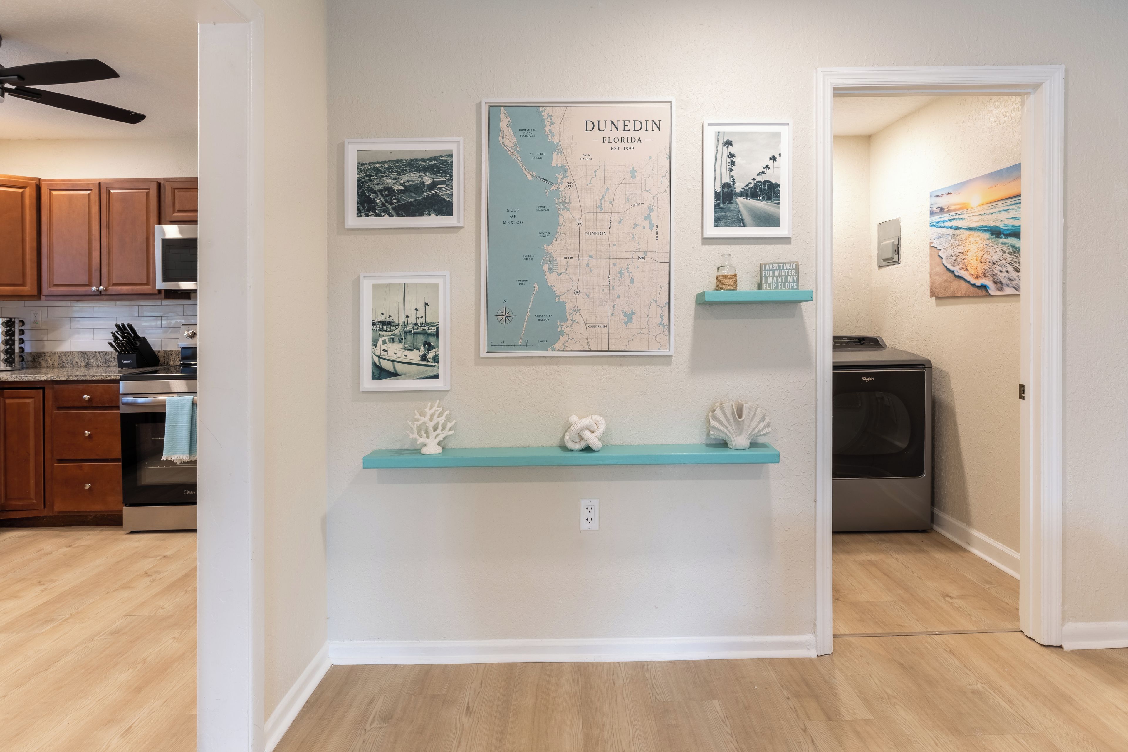 Une cuisine avec des meubles en bois, un four à micro-ondes et un réfrigérateur. Les murs sont ornés de cartes et de photos encadrées, et une petite étagère expose quelques objets décoratifs.