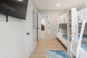 Une chambre avec des lits superposés, un téléviseur à écran plat et un couloir menant à une autre pièce.