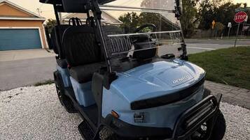 A golf cart parked on a gravel driveway with a garage in the background.