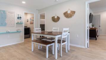 A dining area with a wooden table and white chairs, a map on the wall, and a kitchen in the background.