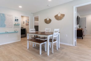 A dining area with a wooden table and white chairs, a map on the wall, and a kitchen in the background.
