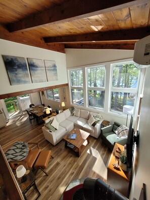 A spacious living area with a wooden ceiling, large windows, and a dining area with a table set for four. - China Lake Chalet with Private Waterfront & Dock (China)