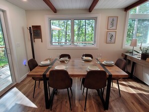 A dining room with a wooden table set for six, surrounded by chairs, with a window providing a view of trees. - China Lake Chalet with Private Waterfront & Dock (China)