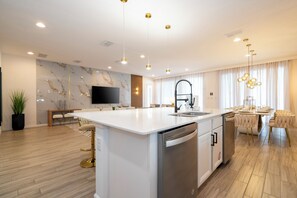 A modern kitchen with a central island, a dining area with a chandelier, and a living space with a flat-screen TV. - The best 9-suite house at Sonoma Resort (Kissimmee)