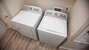 Två tvättmaskiner av märket Whirlpool, med frontmatning, står i ett tvättrum med trägolv och en vit dörr.