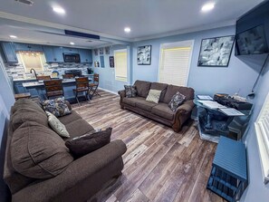 A living room with a sofa set, a coffee table, and a dining area with chairs. There is a kitchen in the background with a microwave and a coffee machine. - Livingston Retreat w/ Covered Patio & Yard (Livingston)