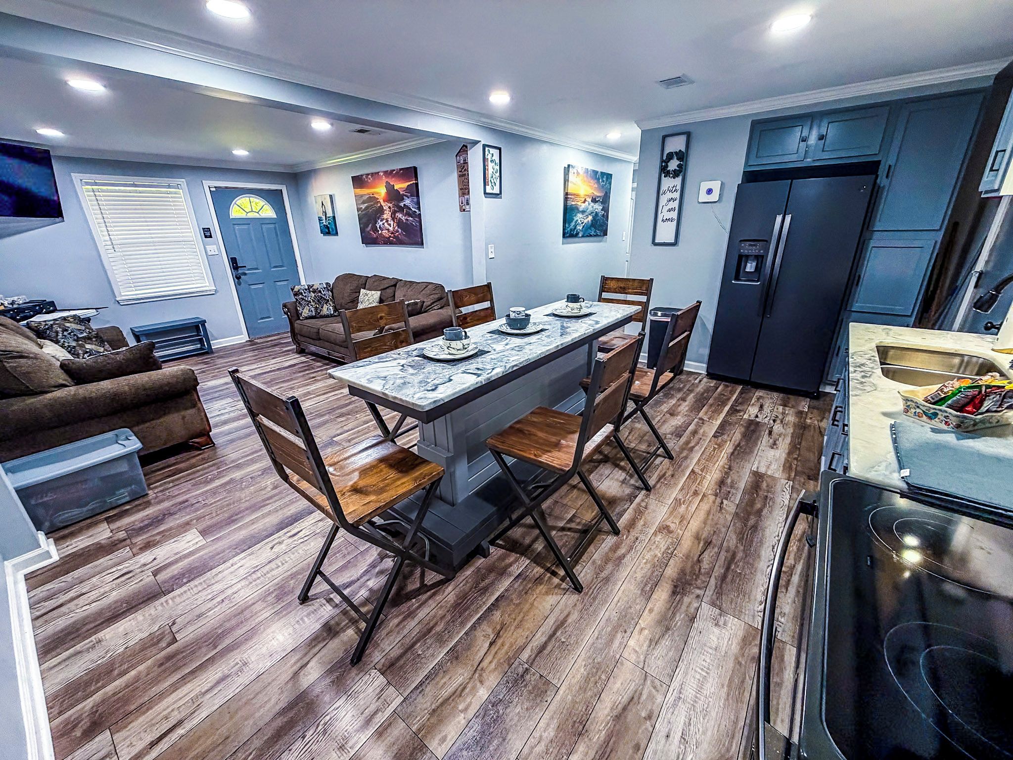 A modern kitchen with a built-in refrigerator, a dining area with a marble table, and a living room with a sofa and a TV.