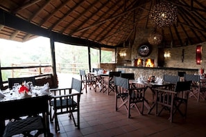 An outdoor dining area with wooden tables and chairs, a stone wall, and a fire feature. - Valley Lodge Conference and Spa (Magaliesburg)