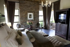 A modern living room with a stone wall, a sofa, a TV, and a chandelier. - Valley Lodge Conference and Spa (Magaliesburg)