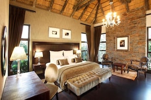 A bedroom with a large bed, bedside tables, a chandelier, and a stone wall. - Valley Lodge Conference and Spa (Magaliesburg)