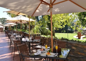 An outdoor dining area with tables and chairs, umbrellas, and a stone wall. - Valley Lodge Conference and Spa (Magaliesburg)