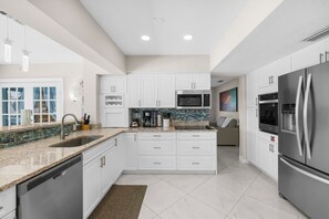 A modern kitchen with white cabinetry, stainless steel appliances, and a tiled backsplash. - Pelican Point Waterfront Heated Pool Tiki (Plantation)