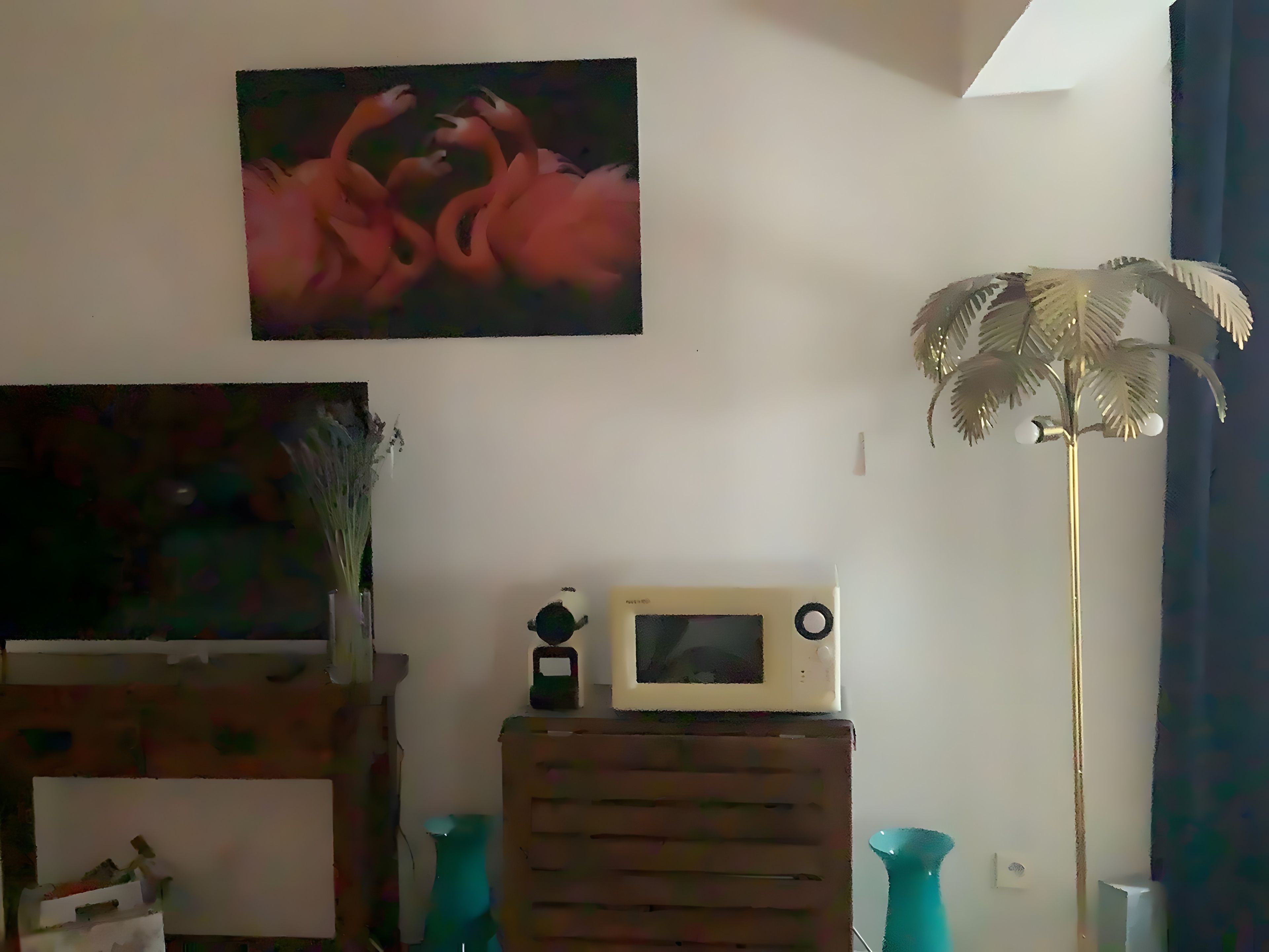 Une pièce avec un tableau, une petite table sur laquelle se trouve un micro-ondes, une lampe décorative et un vase.