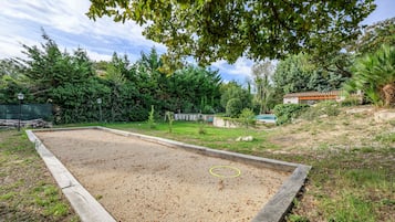A gravel court with a wooden border, surrounded by greenery and trees.