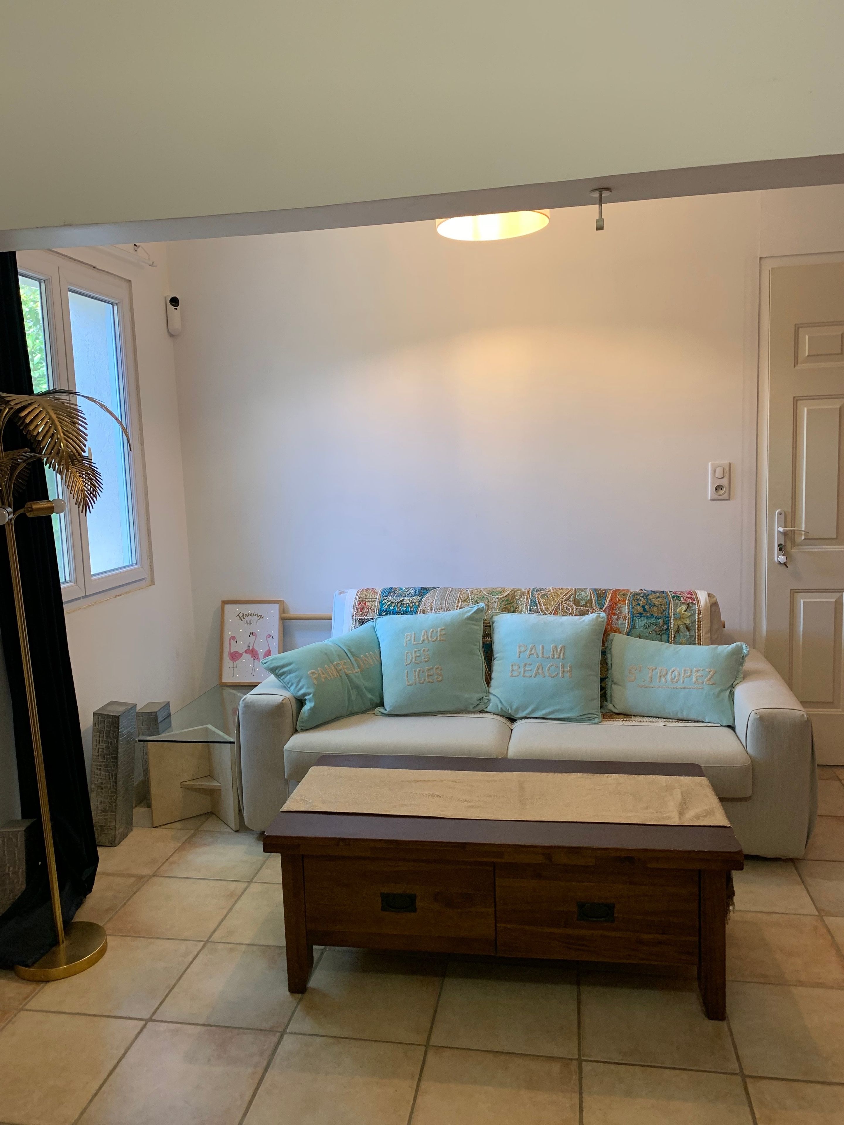 Ein Wohnzimmer mit einem beigefarbenen Sofa, einem Holztisch, einer gemusterten Decke und einer Zierpflanze.