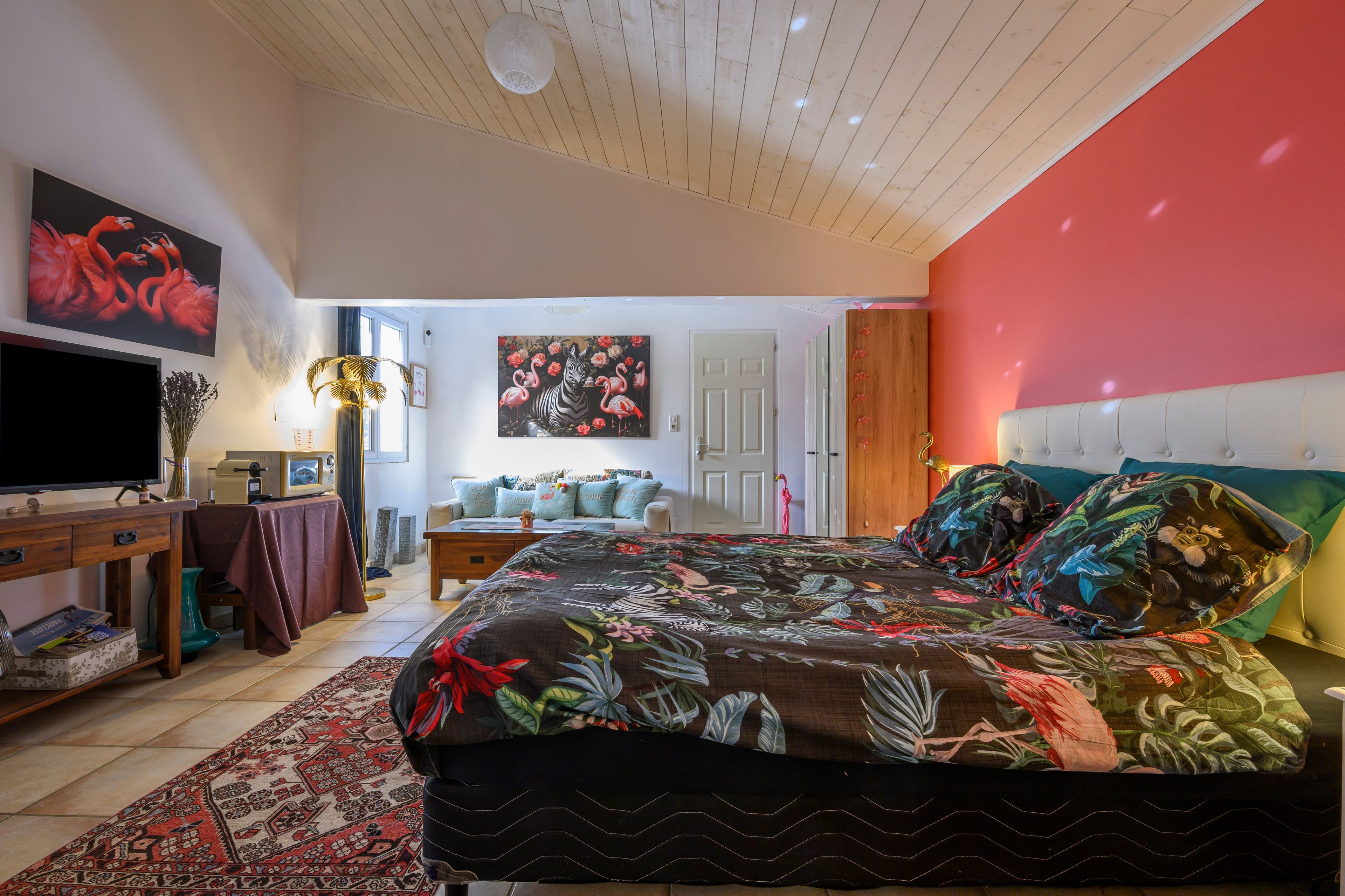 Ein Schlafzimmer mit einem großen Bett, einem Fernseher, einem Schreibtisch und einem Gemälde mit Flamingos und einem Zebra.