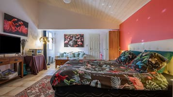 Een slaapkamer met een groot bed, een televisie, een bureau en een schilderij van flamingo's en een zebra.