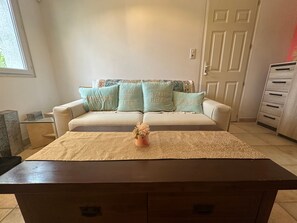 A living room with a sofa, a coffee table, and a door in the background. - Holiday Home 'Les Flamants Roses' with Shared Pool, Private Terrace and Wi-Fi (Caumont-sur-Durance)