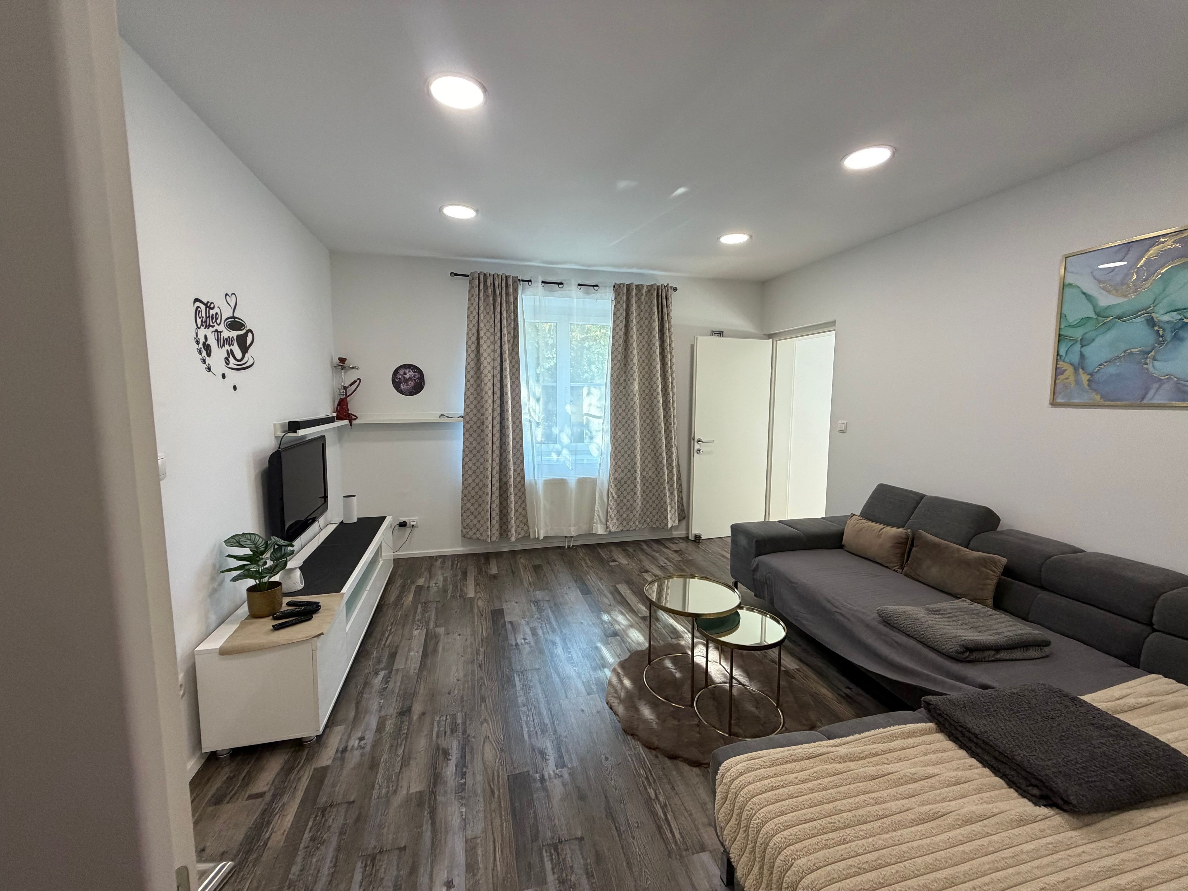 A modern living room with a sofa, a TV, and a coffee-themed wall decoration.