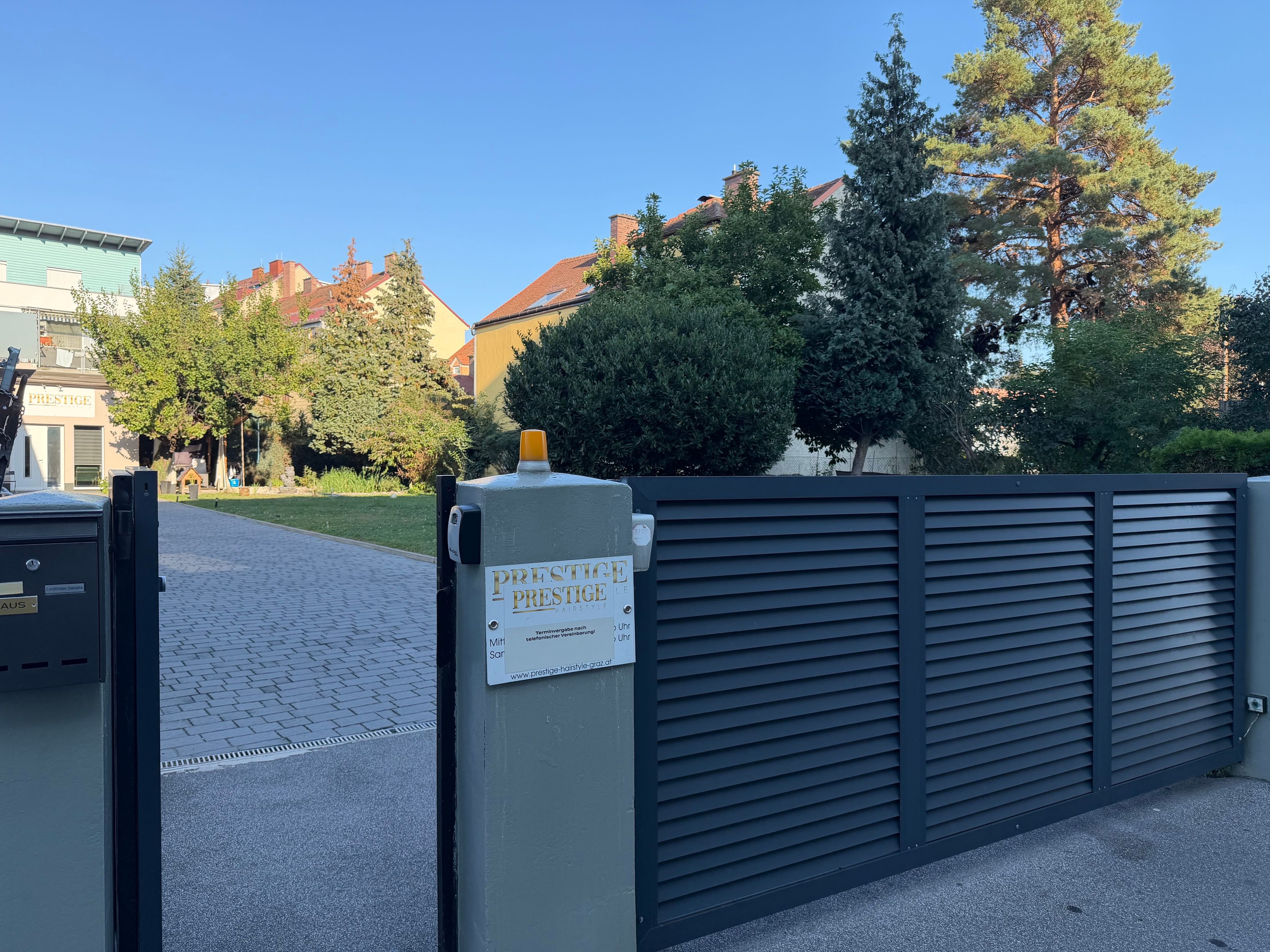 A gated entrance with a sign for 'Prestige Prestige Hair Salon' and a building with a brick facade in the background.