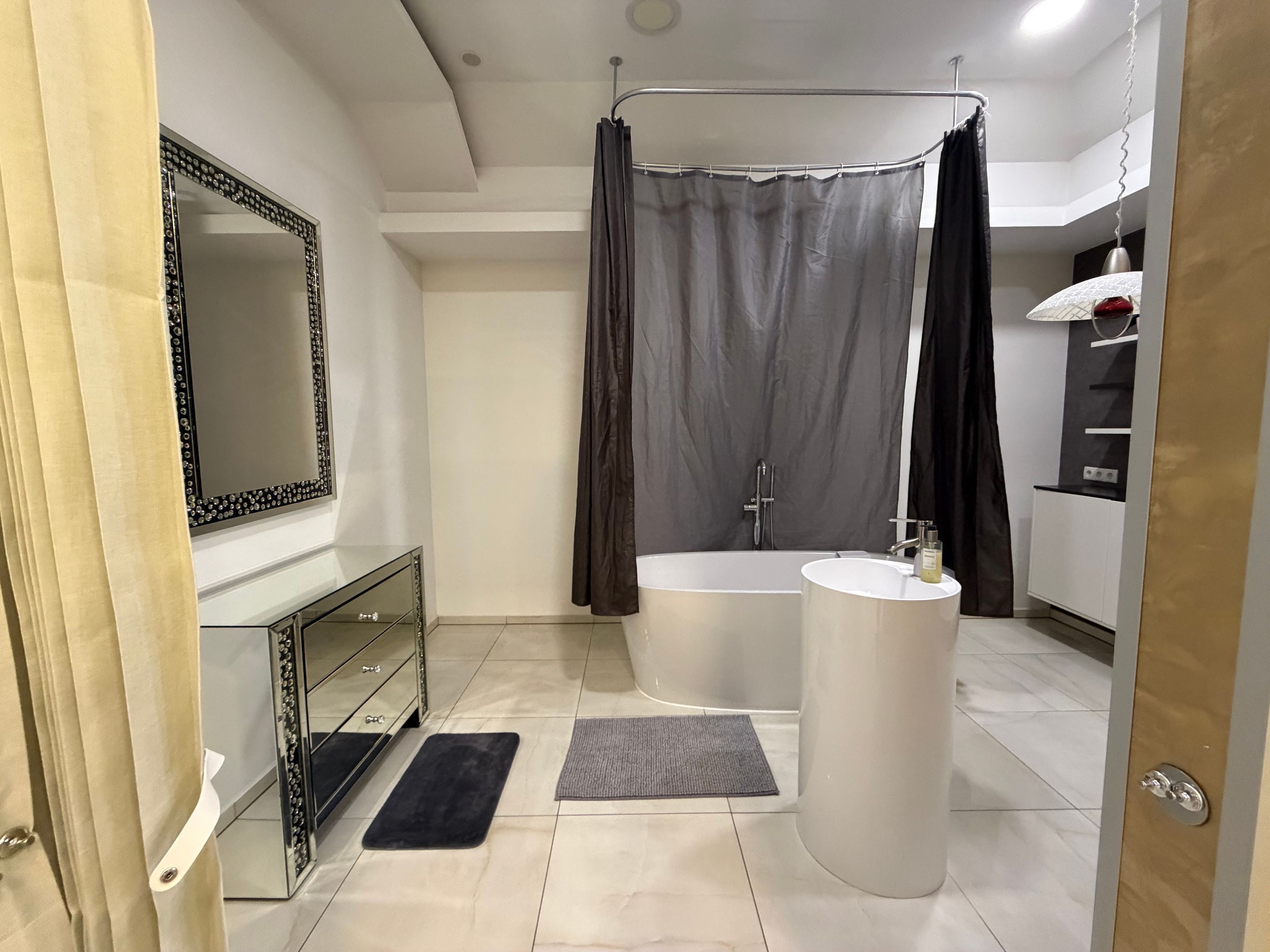 Uma casa de banho moderna com banheira, toucador com espelho e cortina de chuveiro.