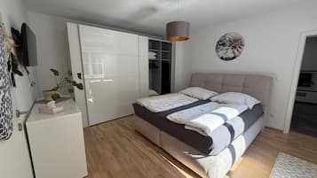 A bedroom with a bed, bedside tables, a wardrobe, a plant, and a wall-mounted TV.