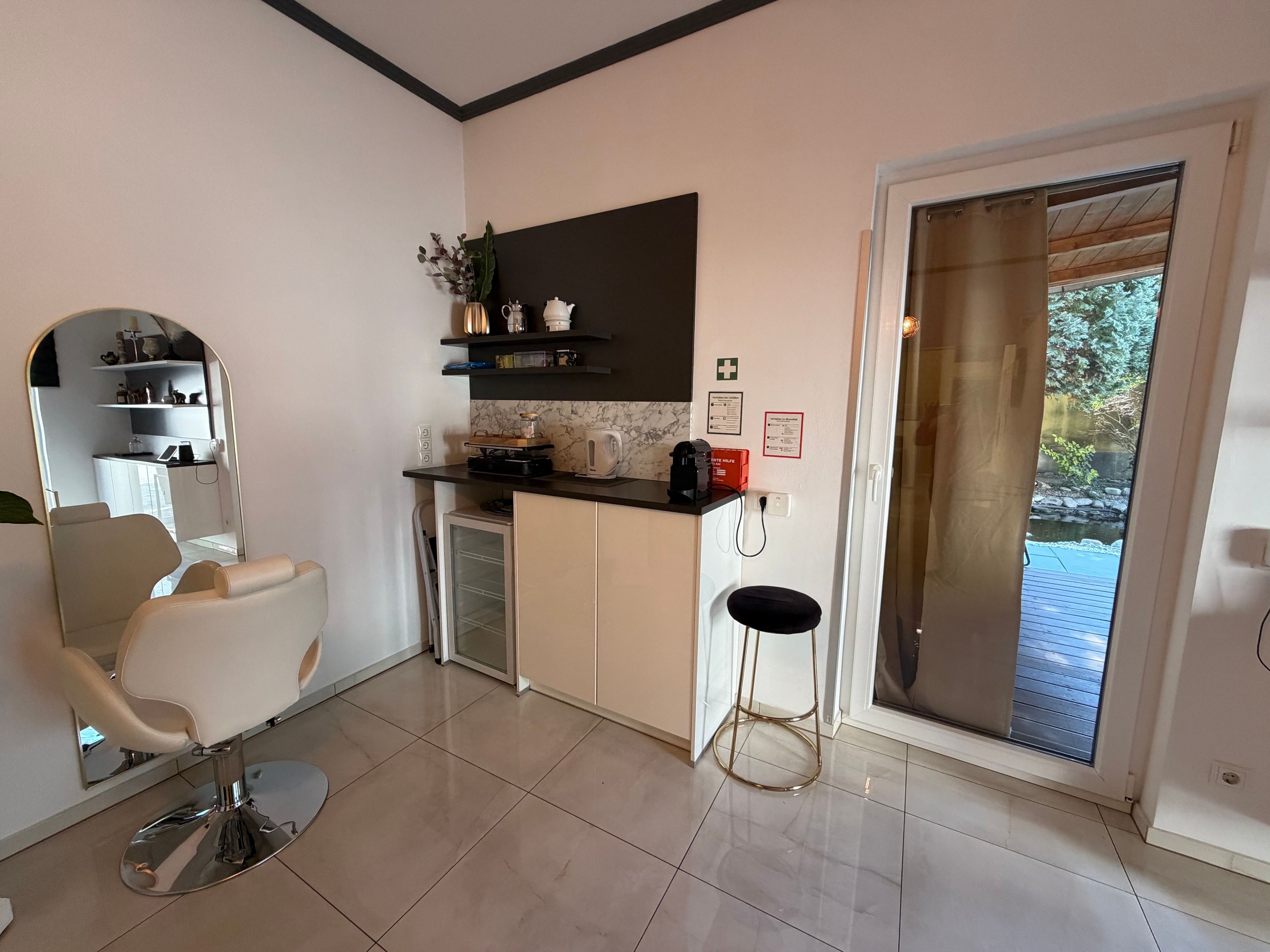 A modern kitchen with a built-in oven, a coffee machine, and a small dining area with a chair and table.