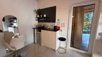 A modern kitchen with a built-in oven, a coffee machine, and a small dining area with a chair and table.