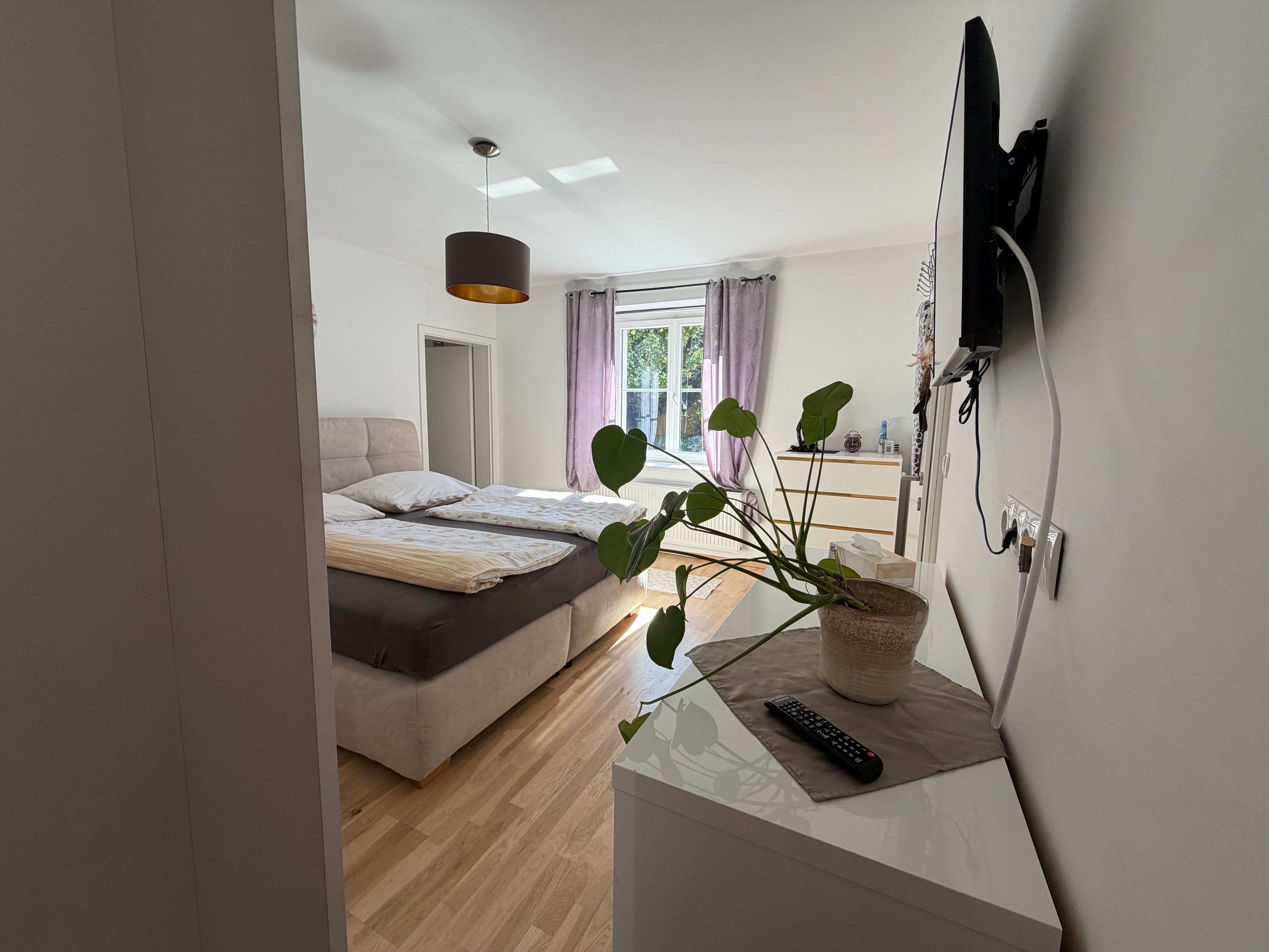 A modern bedroom with a bed, bedside table, and a television mounted on the wall.
