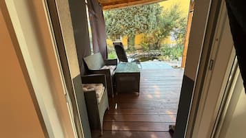 Una terraza de madera con zona de estar, que incluye un sofá y una silla, que da a un jardín con un estanque.