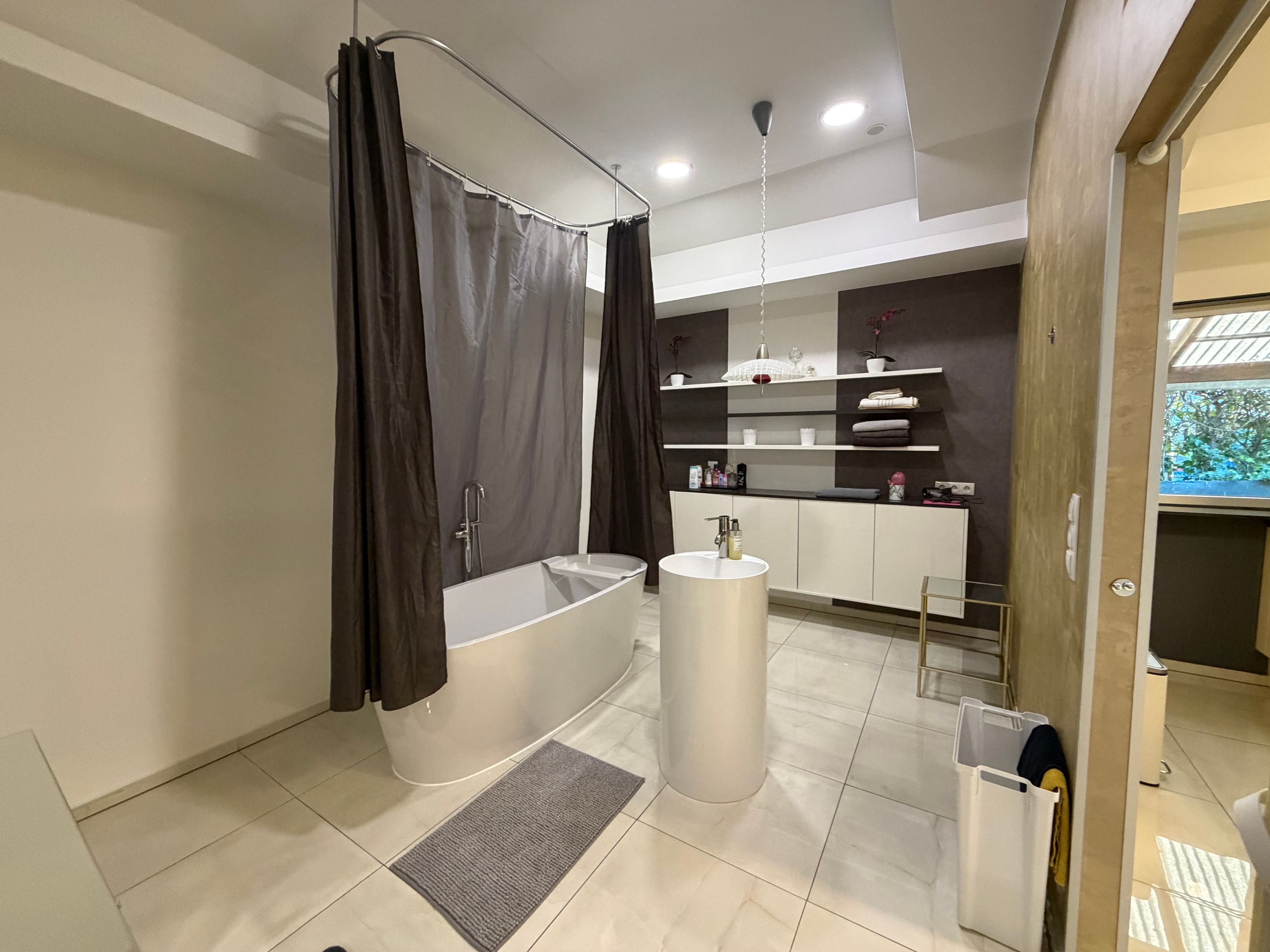 A modern bathroom with a freestanding bathtub, a pedestal sink, and a shower area.