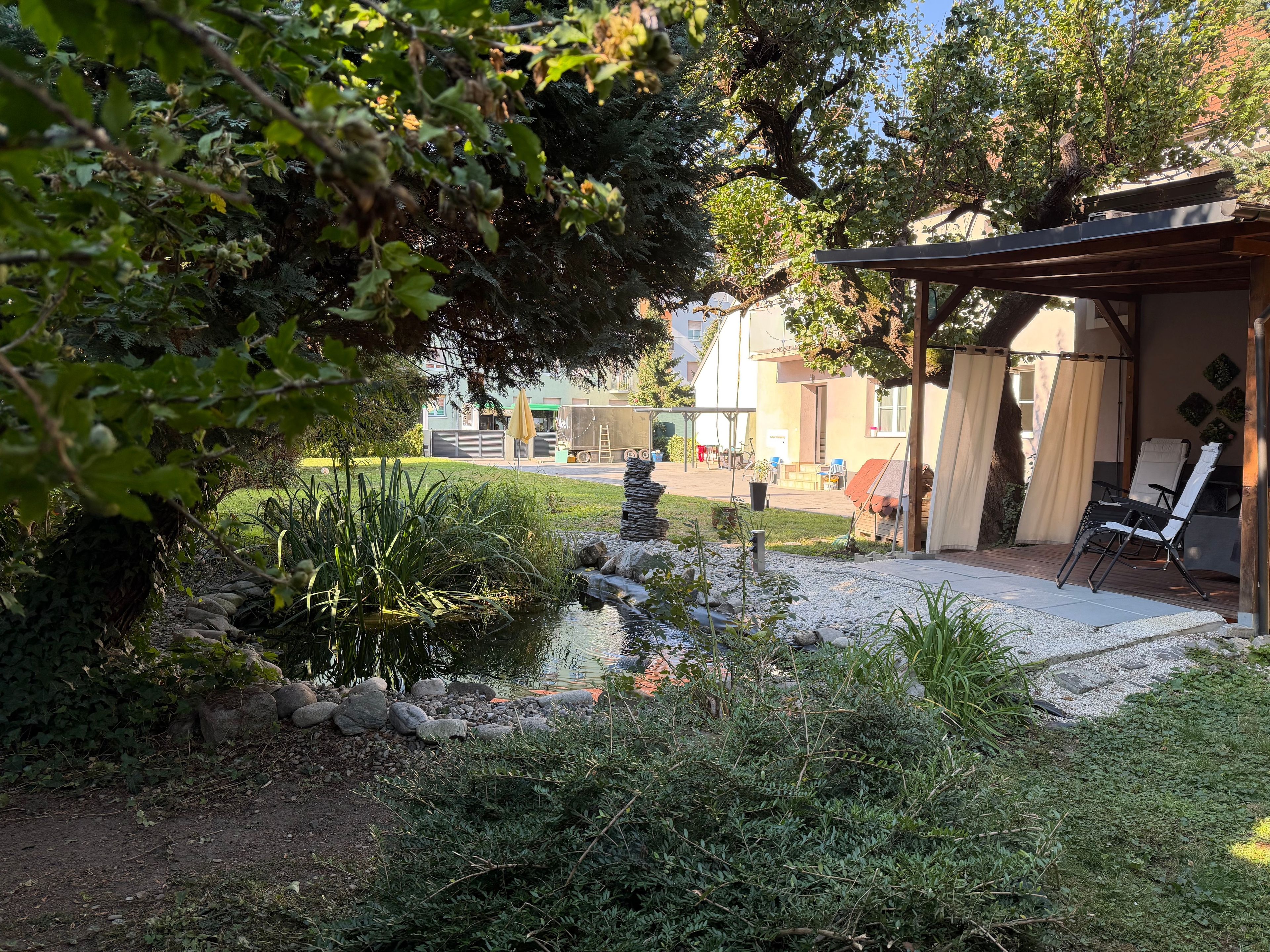 A garden with a pond, outdoor seating, and a building with a covered patio.