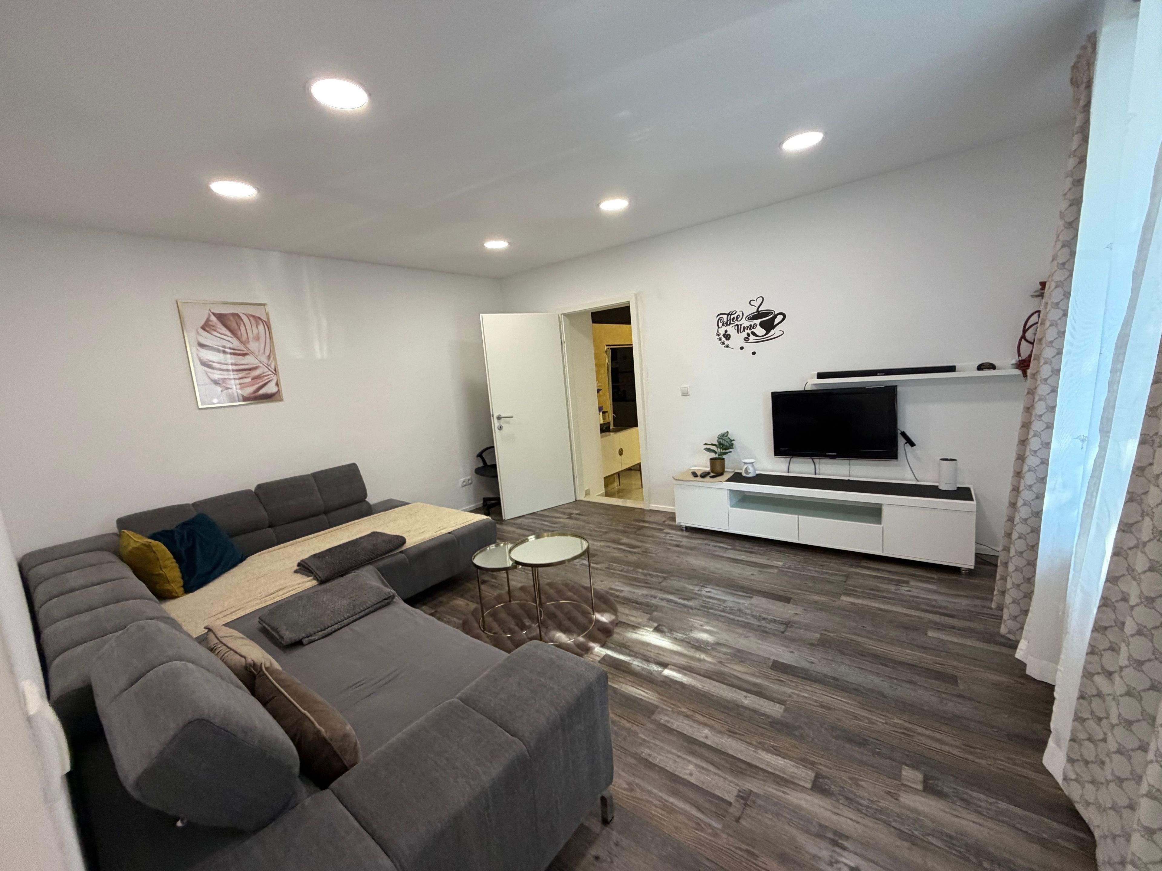 A modern living room with a sectional sofa, a flat-screen TV, and a coffee-themed wall decal.