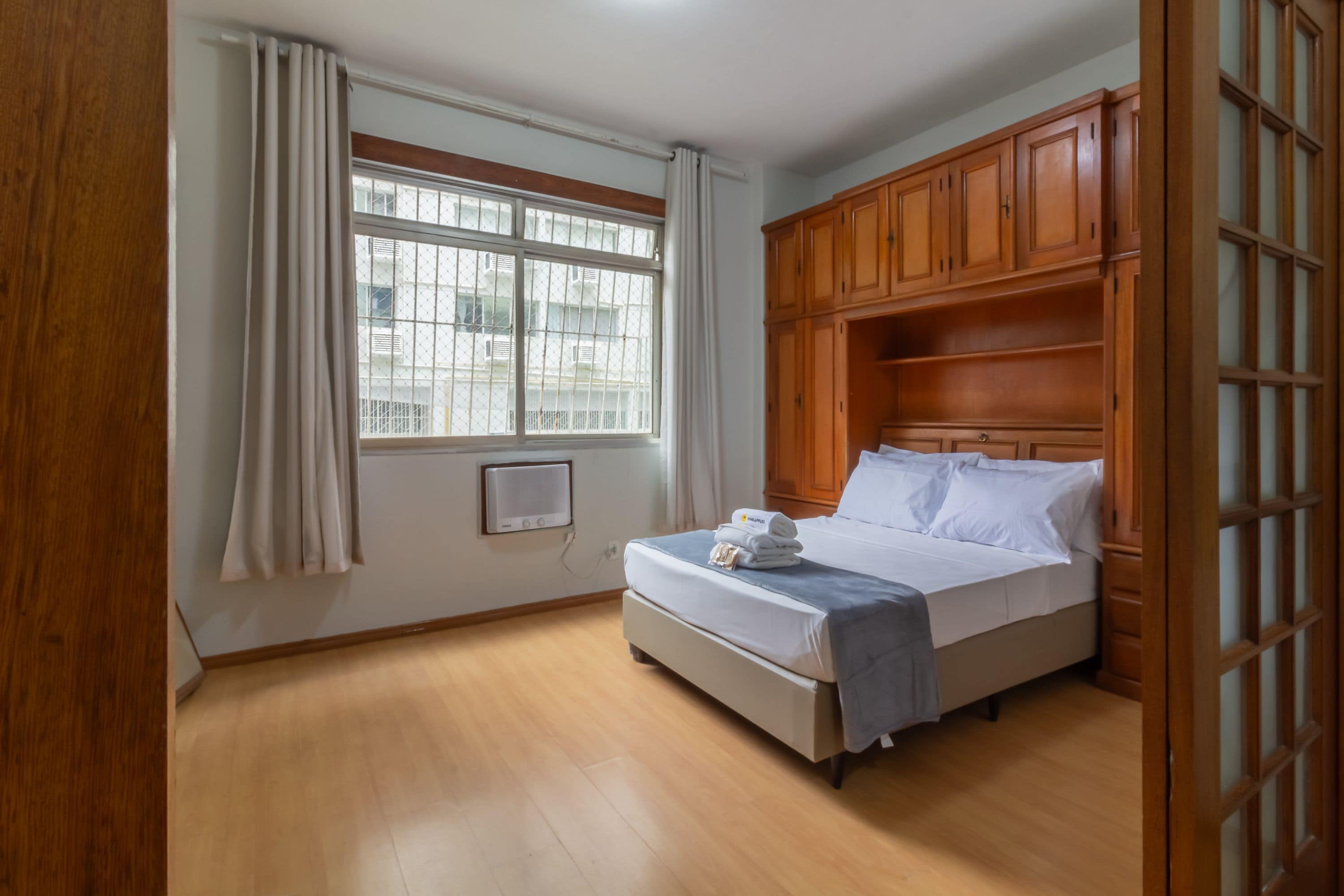 Ein Hotelzimmer mit einem Bett, einem Holzschrank, einem Fenster mit Vorhängen und einer Wand-Klimaanlage.