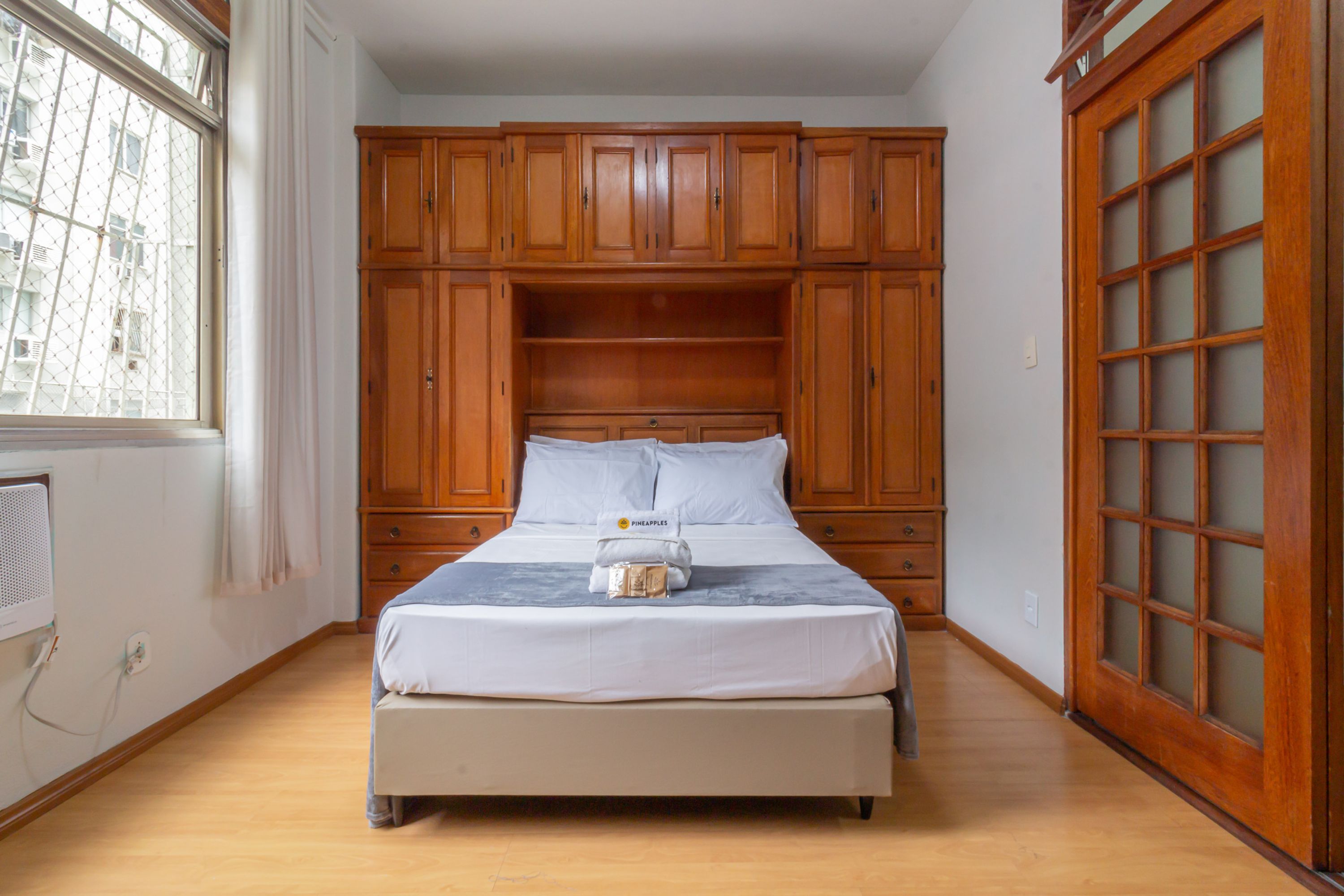 A bedroom with a bed, wooden wardrobe, and a window.